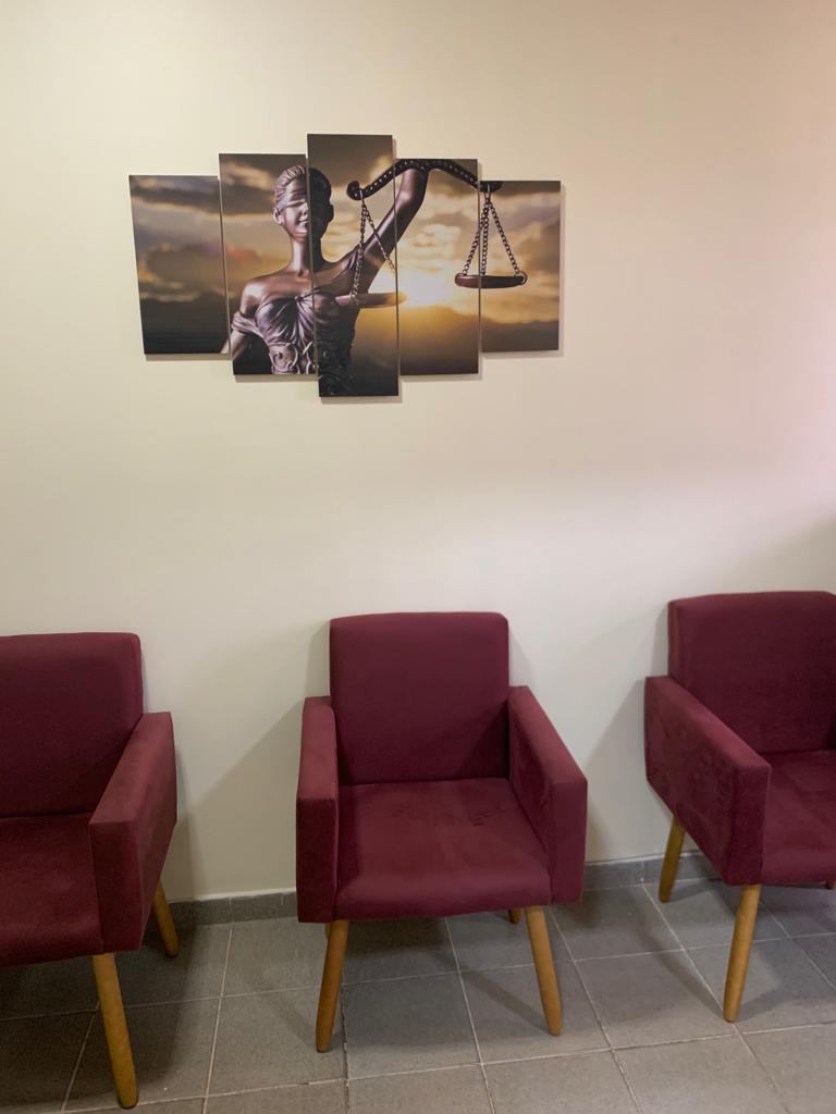 Sala de espera do escritório com poltronas vermelhas e quadro da justiça na parede